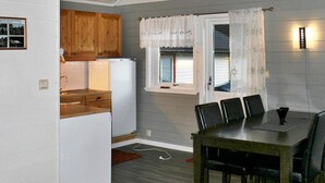Eine kleine Küche mit Holzausstattung, einem weißen Kühlschrank, einem Esstisch mit vier Stühlen und einem Fenster mit Vorhängen.