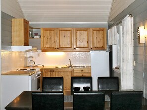 A compact kitchen with wooden cabinets, a white refrigerator, a sink, and a dining area with four chairs. - 7 Person Holiday Home in Selje (Stad)