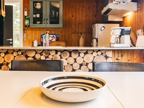 A kitchen with a wooden wall, a refrigerator, a coffee maker, and a bowl on the table.