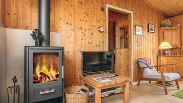 A cozy room with a wood-burning stove, a television, a chair, and a small table with a basket.