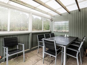 A covered outdoor dining area with a table and chairs, large windows, and a view of trees. - 6 Person Holiday Home in Thisted (Thisted)