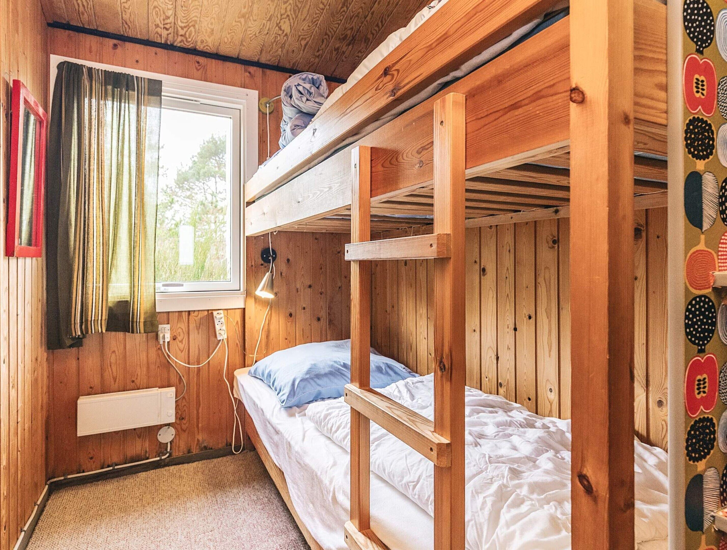 Een slaapkamer met een stapelbed, houten wanden, een raam met gordijnen, een bedlampje en een stopcontact.