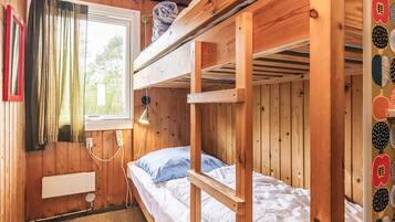 Een slaapkamer met een stapelbed, houten wanden, een raam met gordijnen, een bedlampje en een stopcontact.