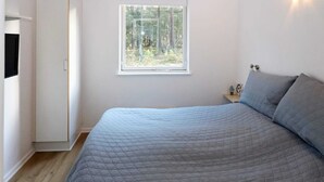 A bedroom with a bed, a window with a view of trees, a bedside table with a lamp, and a wardrobe. - Lovely Holiday Home with Terrace near Hadsund (Hadsund)