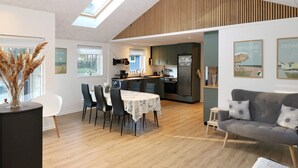 A modern living room with a dining area, a grey sofa, and a kitchen in the background. - Lovely Holiday Home with Terrace near Hadsund (Hadsund)