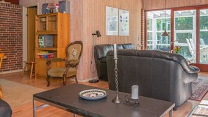 A cozy living room with wooden walls, a leather sofa, a wooden cabinet, and a dining area with a table and chairs. - 6 Person Holiday Home in Orsted-by Traum (Ørsted)