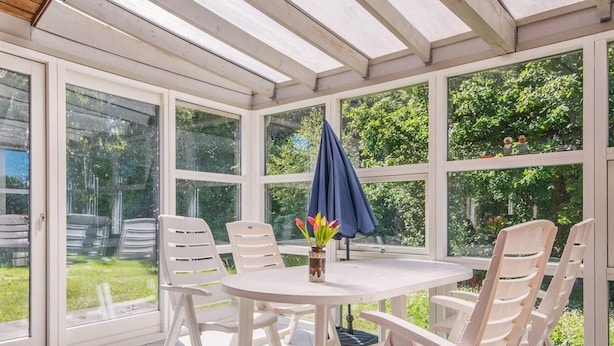 A sunroom with a tiled floor, white furniture, and large windows offering a view of the garden. - 6 Person Holiday Home in Orsted-by Traum (Ørsted)