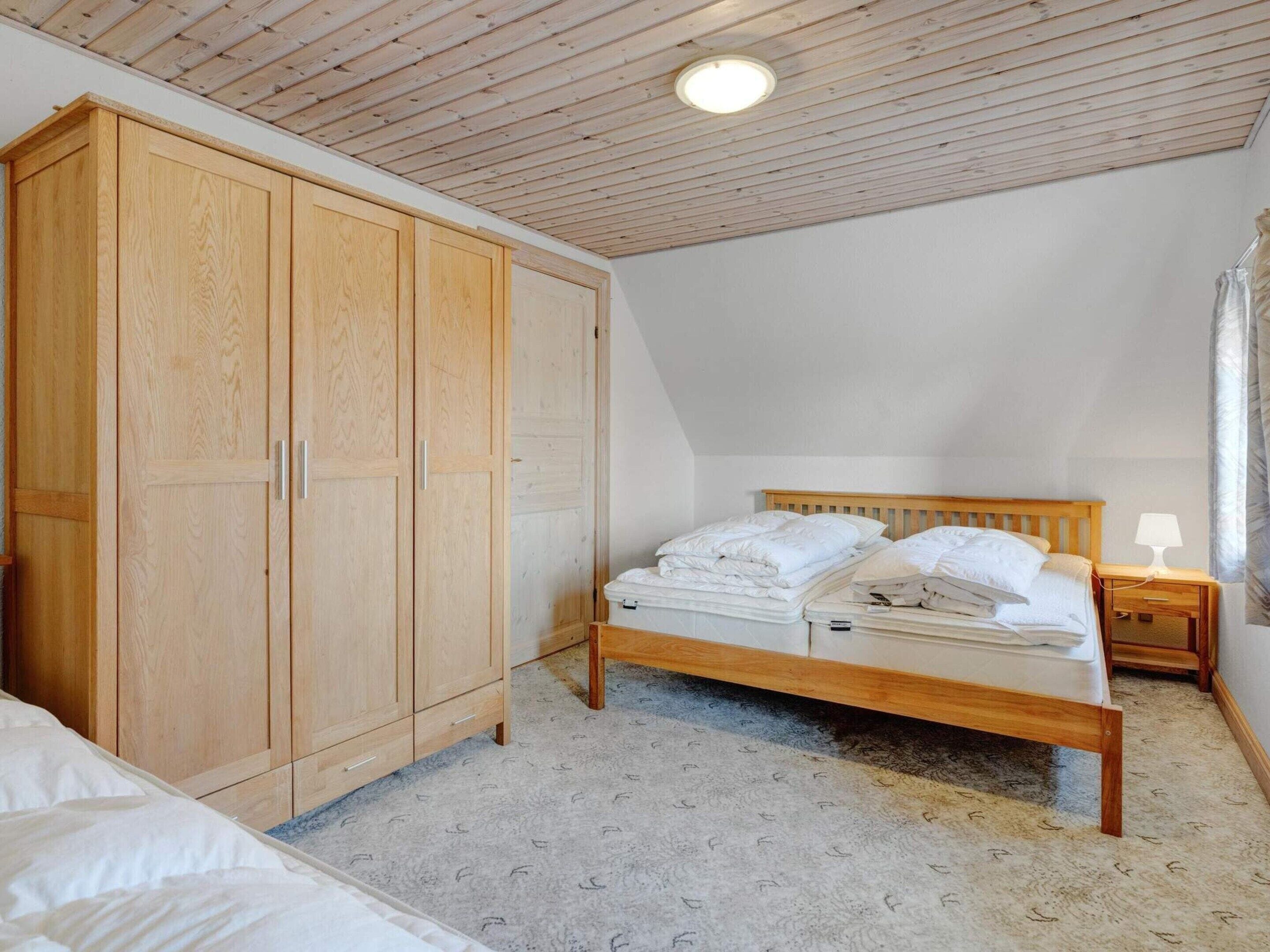 Un dormitorio con un armario de madera, una cama con ropa blanca, una mesita de noche y una lámpara en el techo.
