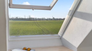 Una stanza con una finestra che si affaccia su un campo verde e un cielo sereno.