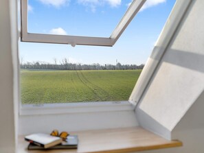 Una habitació amb finestra que dona a un camp verd i un cel serè.