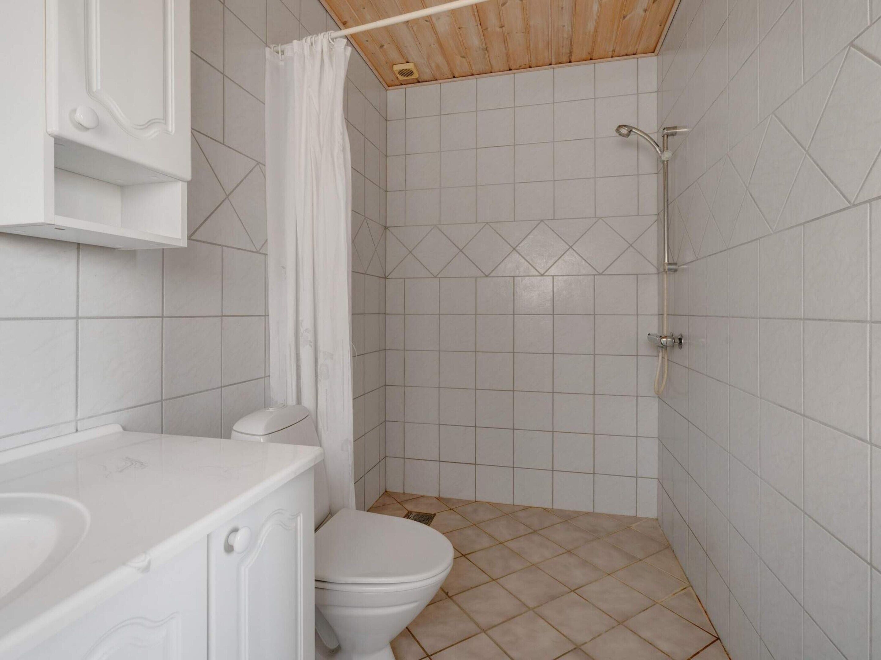 A small, clean bathroom with white tiles, a toilet, a shower, and a bathtub.