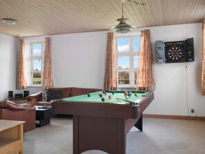 A room with a pool table, a leather sofa, a dartboard, and a window with curtains.