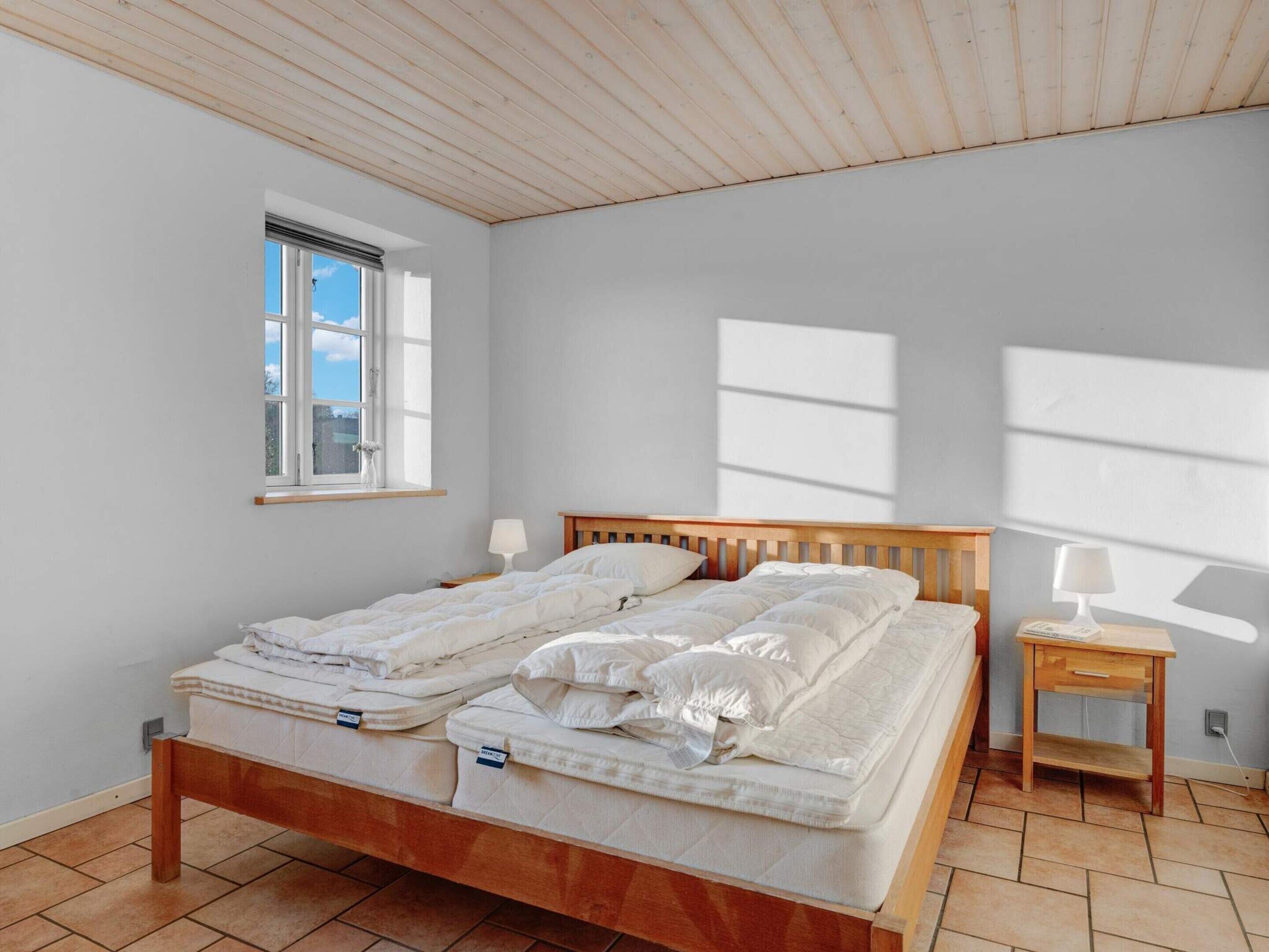 Une chambre avec un lit en bois, deux tables de chevet, une fenêtre et une vue sur le ciel.