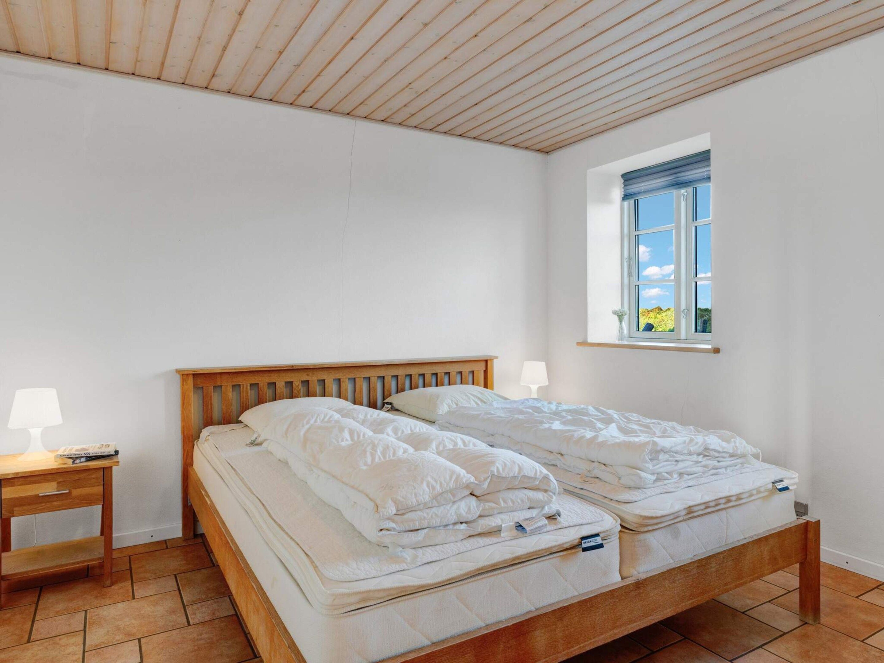 Une chambre à coucher avec un lit en bois, deux tables de chevet avec des lampes, une fenêtre donnant sur un beau paysage et un plancher carrelé.