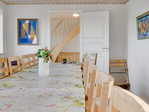 Un comedor con mantel floreado, sillas de madera, un jarrón con flores y una escalera al fondo.