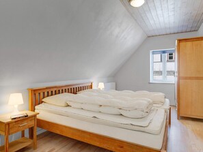 A bedroom with a wooden bed, a nightstand with a lamp, a window with a view of the outside, and a wooden wardrobe.