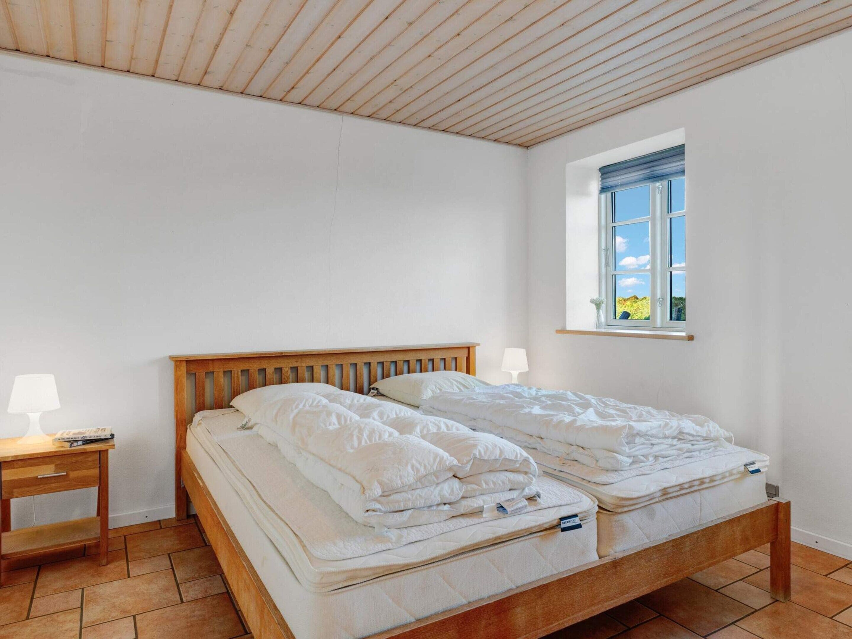 A bedroom with a wooden bed, two bedside tables, a window with a view, and a tiled floor.