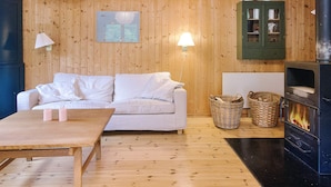 Ett mysigt rum med trägolv, en vit soffa, ett träbord, ett grönt skåp, en öppen spis och en vägglampa.