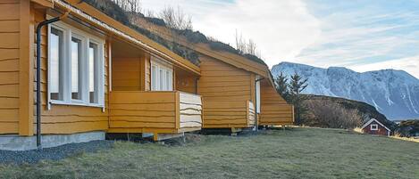 A row of wooden cabins with a grassy field and mountains in the background.