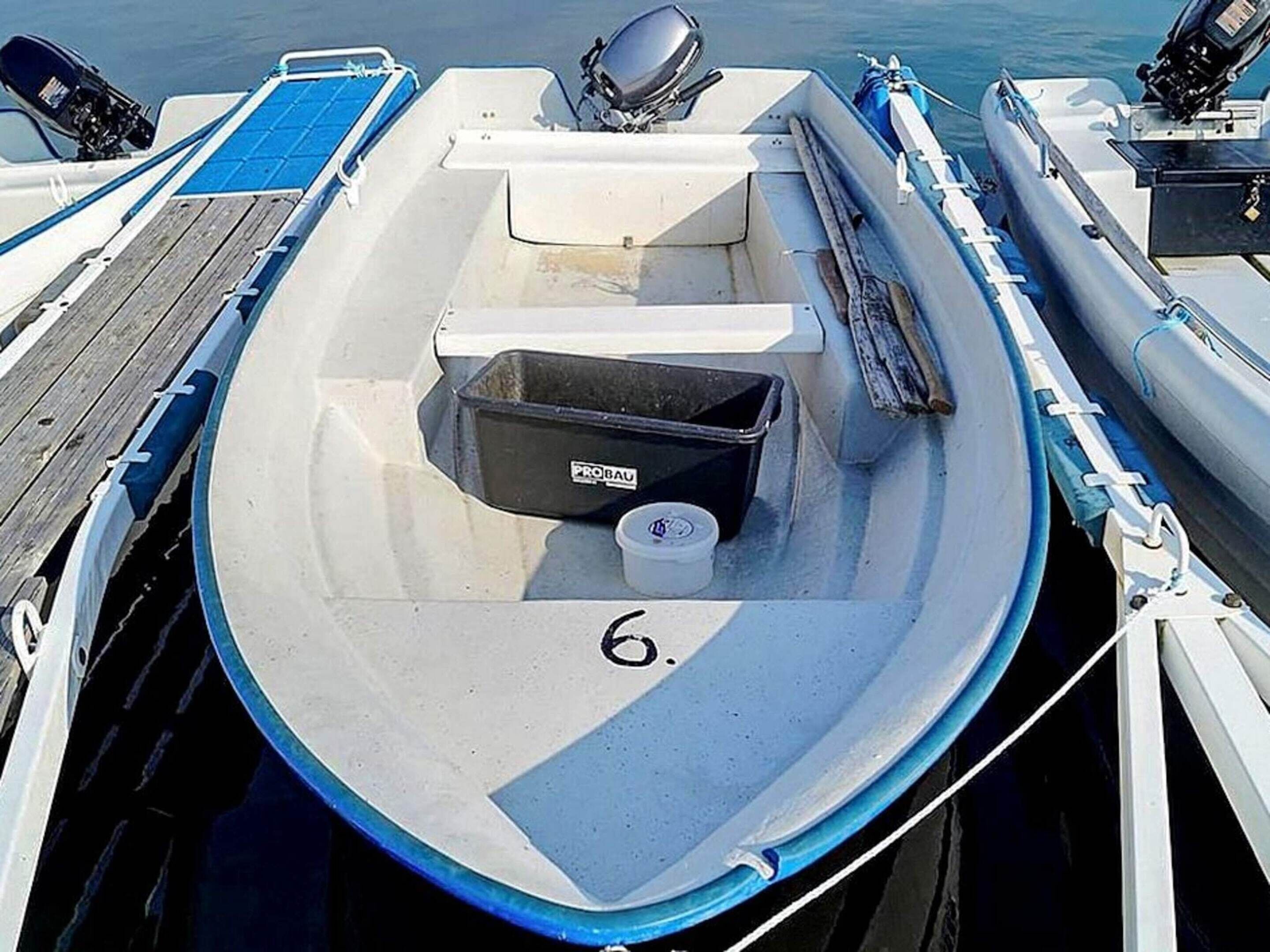 Ein kleines Motorboot liegt an einem Steg, mit der Nummer '6' an der Seite, einem schwarzen Behälter mit der Aufschrift 'PROBAU' und einem blauen Deck.