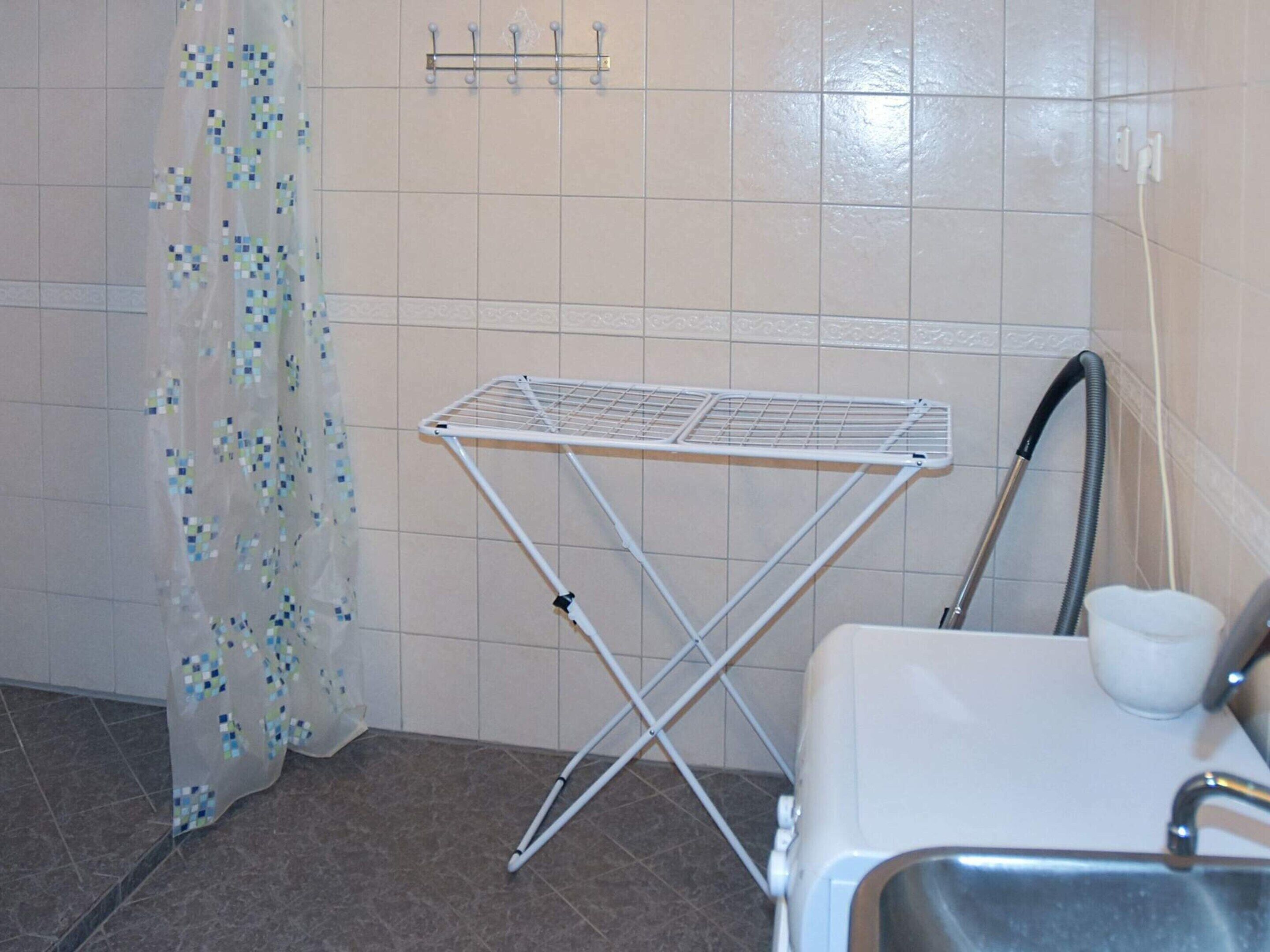 Un baño con un tendedero blanco, una ducha con cabezal de ducha de mano y un lavamanos blanco.