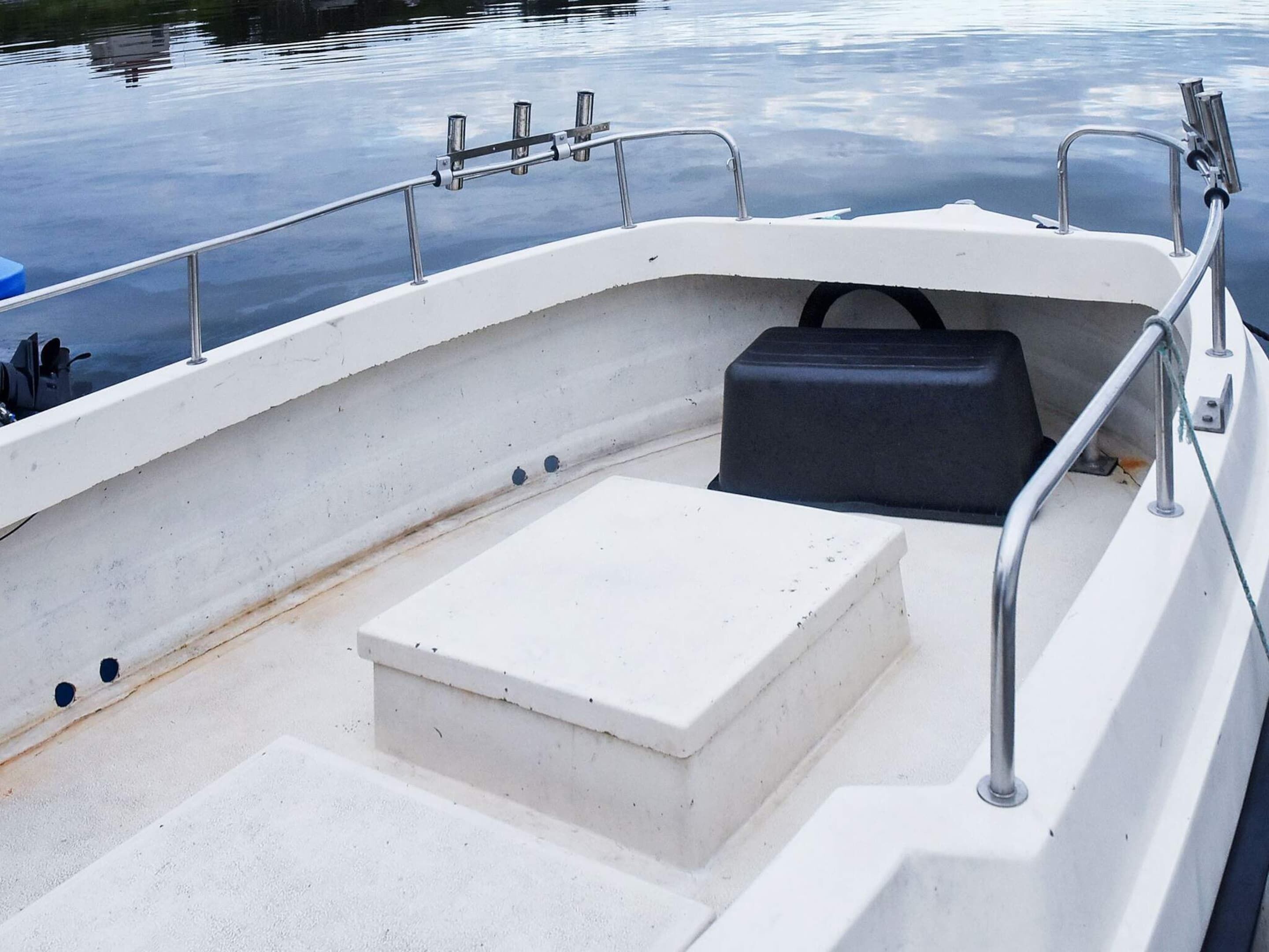 A boat's interior with a white seating area, a black storage compartment, and metal railings.
