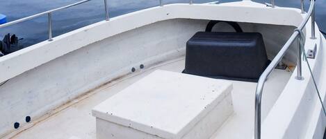A boat's interior with a white seating area, a black storage compartment, and metal railings.