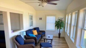 A living room with a ceiling fan, wicker furniture, a coffee table, and large windows.