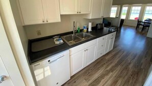 A kitchen with white cabinets, a dishwasher, a sink, and a dining area with a table and chairs.