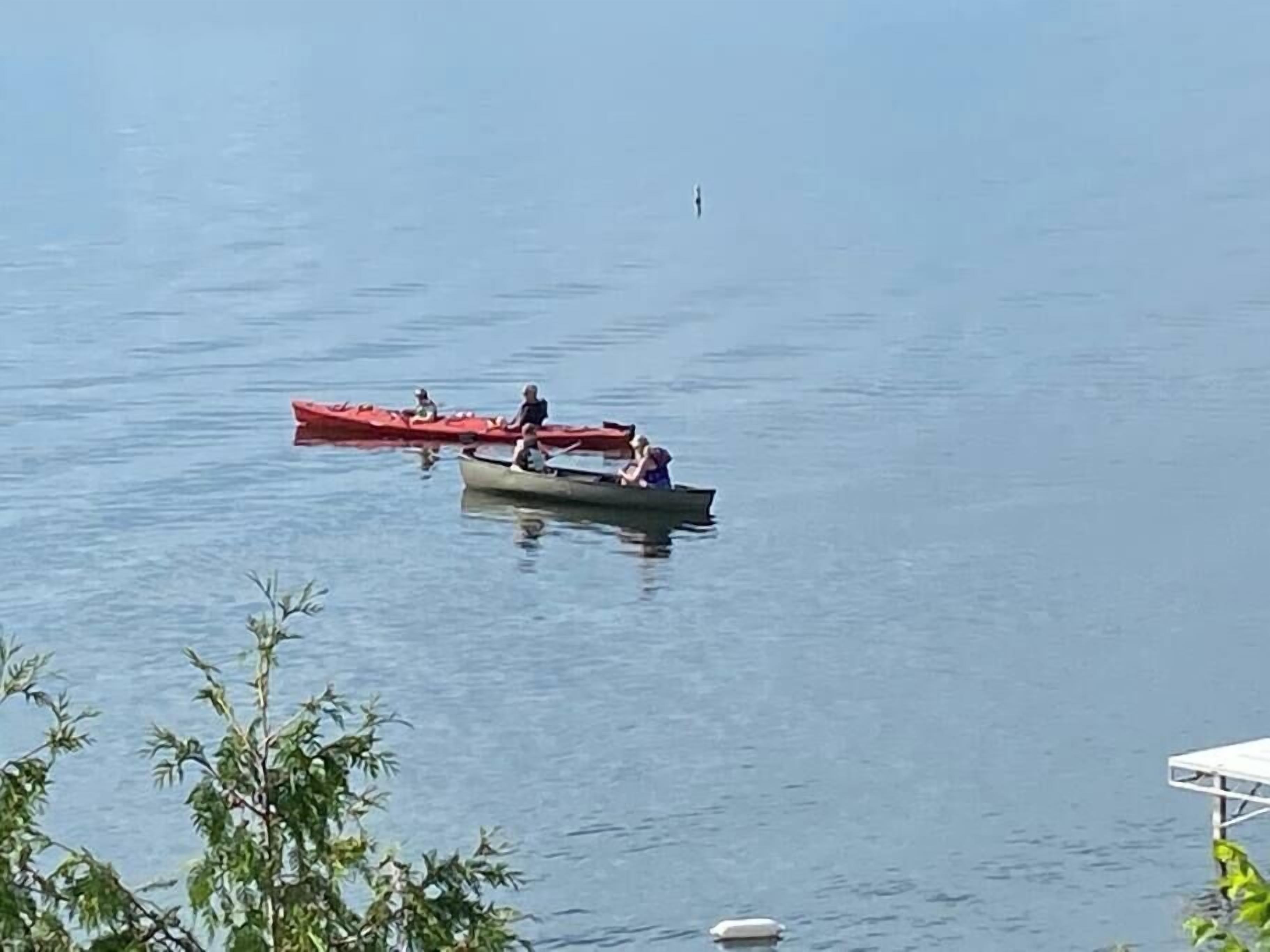 A calm lake with two boats, one red and one green, with people on them.