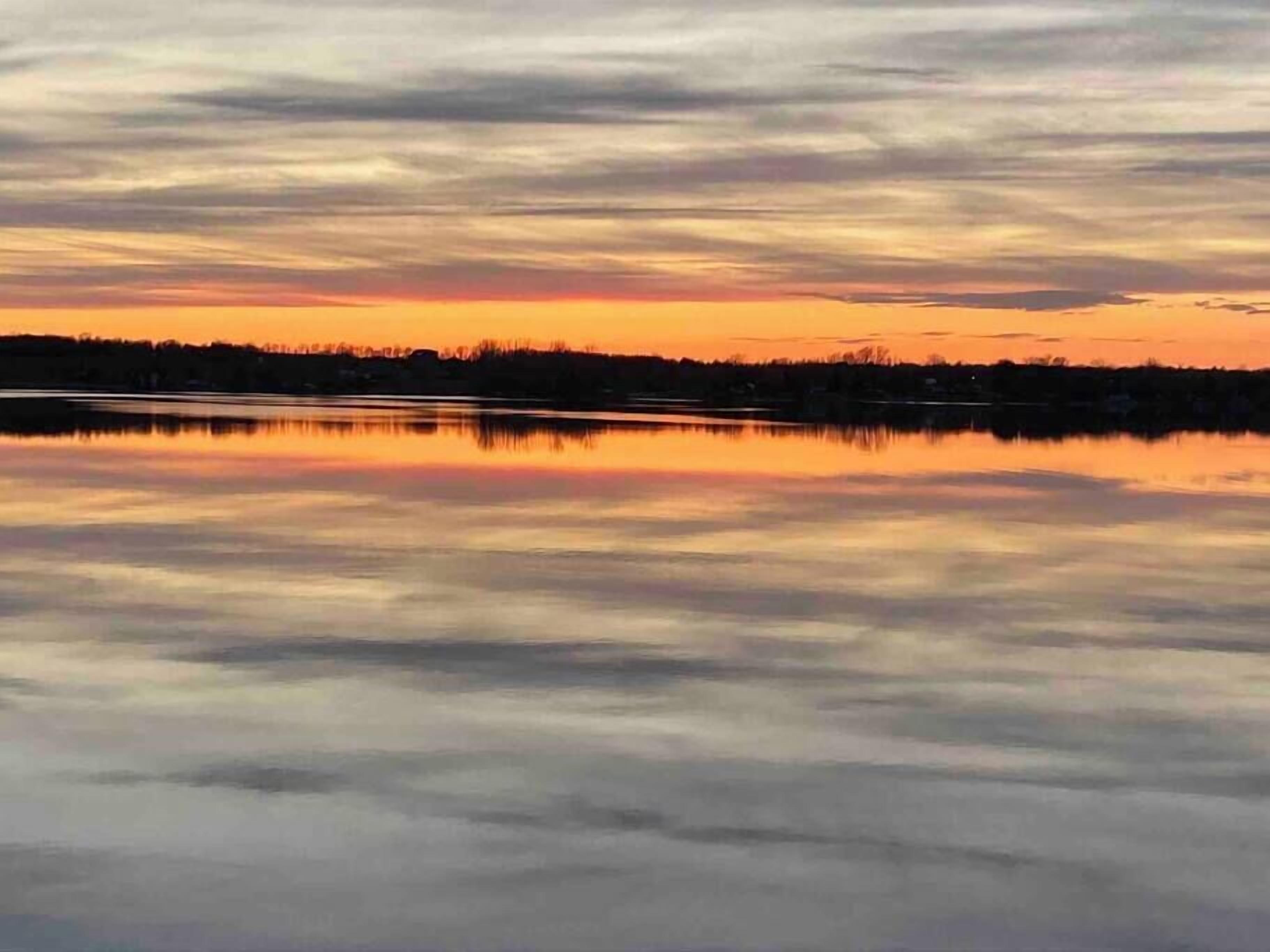 Un lago tranquilo reflejando un cielo al atardecer, con una línea lejana de árboles.