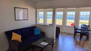 A living room with a dark blue sofa, a small table, and a view of a body of water through large windows.