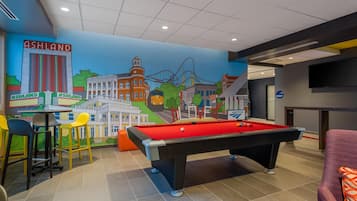 A pool table with a red felt surface, a bar area with stools, and a mural depicting a cityscape with the word 'ASHLAND' on the wall.