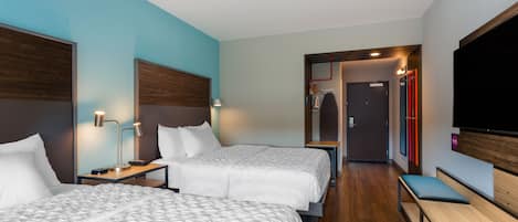 A hotel room with two beds, a bench, a TV, and a mirror.