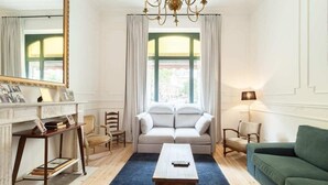 Una sala de estar con un sofá, un sofá verde, una mesa de centro de madera, un espejo y una araña.