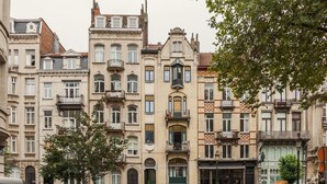 Una hilera de edificios de varios pisos con balcones, una puerta verde y un escaparate con un letrero.