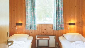 A room with two beds, wooden walls, a window with curtains, and a table. - 6 Person Holiday Home in Gedser-by Traum (Gedser)