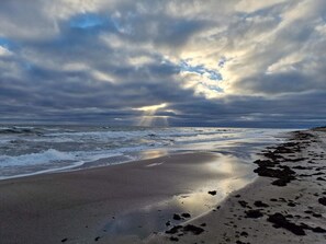 A beach with waves, a cloudy sky, and sunlight breaking through.