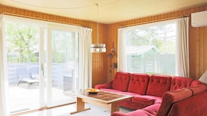 A cozy room with a red sofa, a wooden table, and a sliding glass door leading to an outdoor area. - 6 Person Holiday Home in Gedser-by Traum (Gedser)