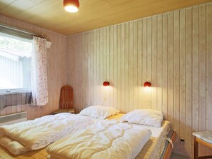 A bedroom with two beds, a wooden headboard, a window with curtains, and wall-mounted lights.
