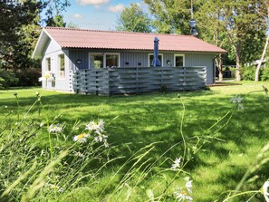 A small, single-story building with a red roof, surrounded by a grassy area with wildflowers.
