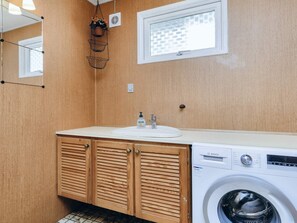 A compact laundry room with a Bosch washing machine, wooden cabinets, a sink, and a window. - 6 Person Holiday Home in Gedser-by Traum (Gedser)