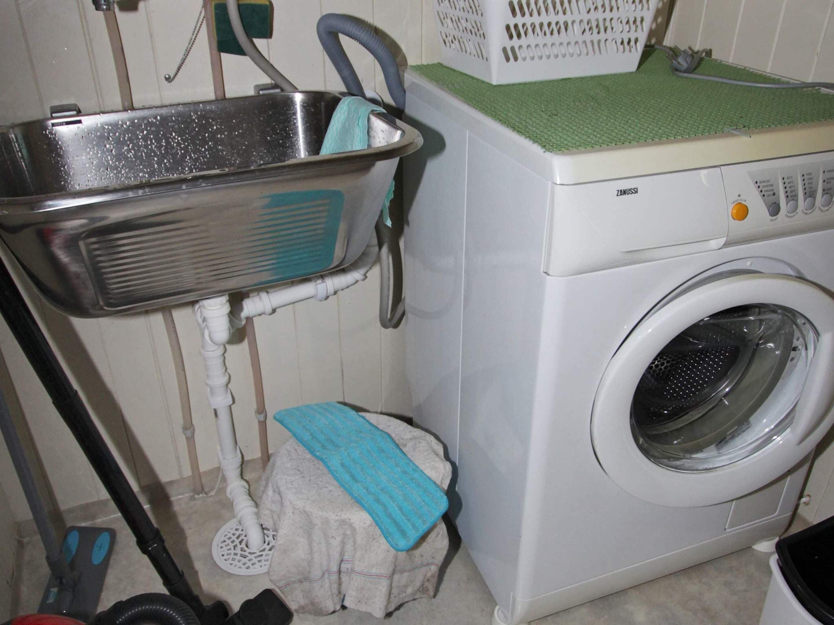 Un espace buanderie comprenant un lave-linge, un évier et un étendoir.
