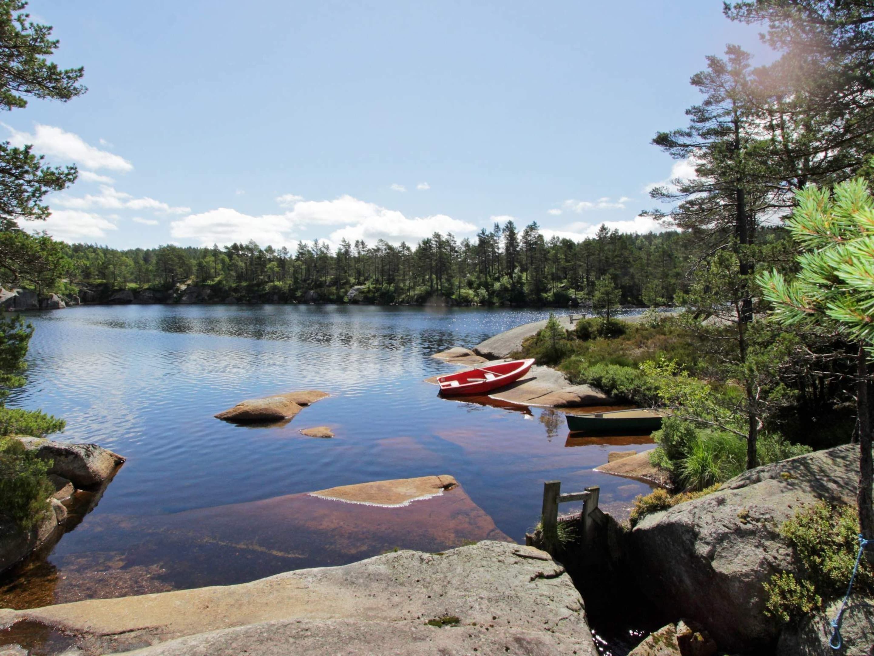A calm lake with boats, surrounded by dense forest and rocky shores.