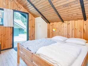 A wooden room with a bed, a door leading outside, and a wall-mounted light fixture.