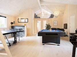 Una habitación con mesa de billar, mesa de futbolín y mesa de ping pong. Una escalera conduce a un nivel superior.