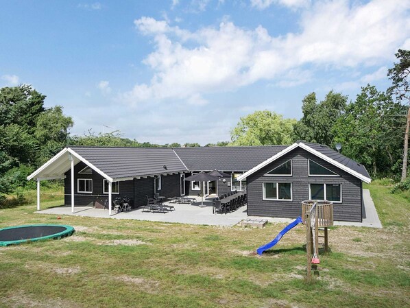 Ein zweistöckiges Haus mit überdachter Terrasse, Trampolin und Rutsche.