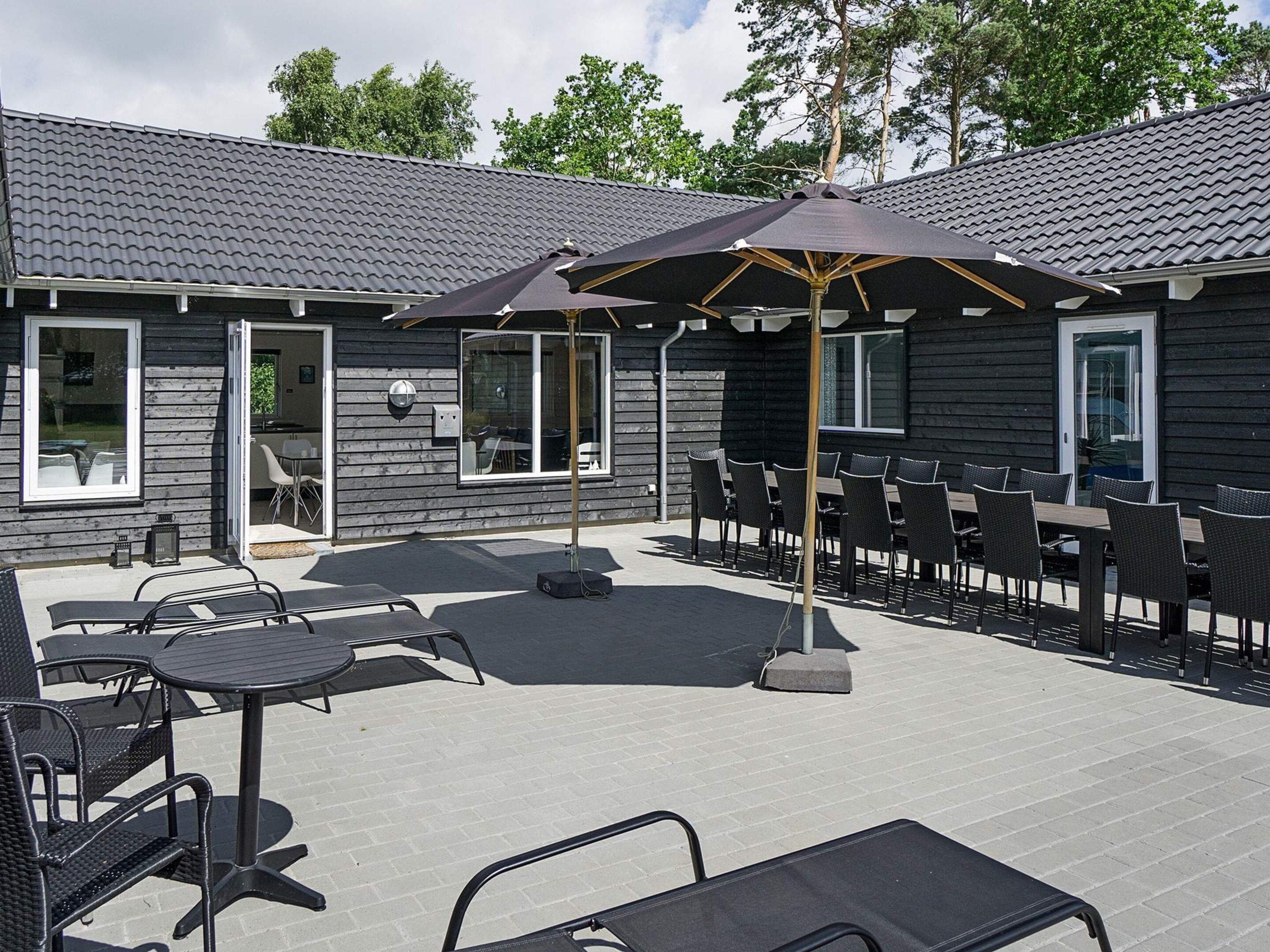 An outdoor patio with tables and chairs, a covered seating area, and a building with a tiled roof.