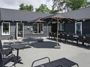 Une terrasse extérieure avec des tables et des chaises, un espace de repos couvert et un bâtiment doté d’un toit en tuiles.