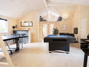 A room with a pool table, a ping pong table, a billiards table, and a staircase leading to an upper level.